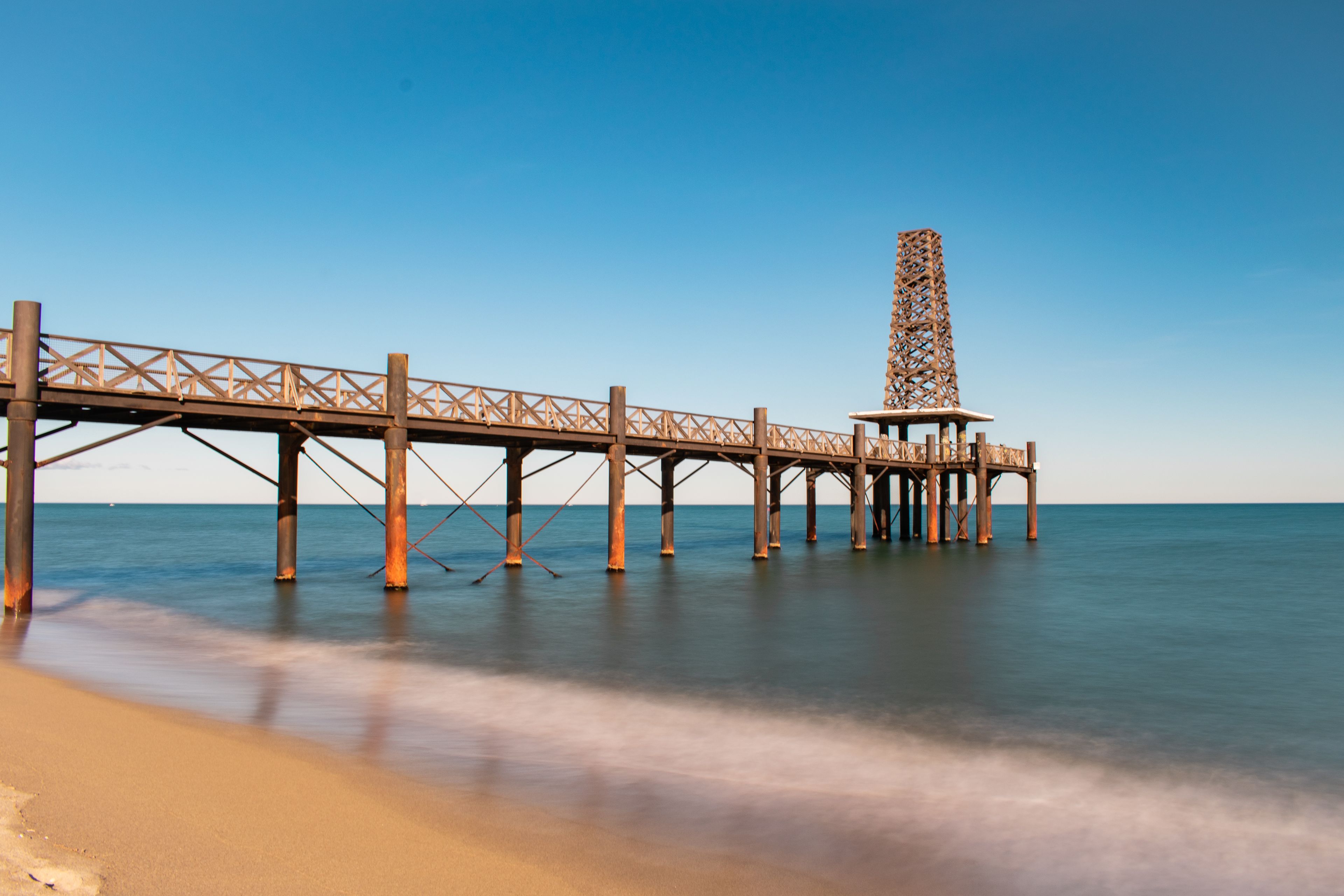 A long pier extending into calm waters with a clear sky above.