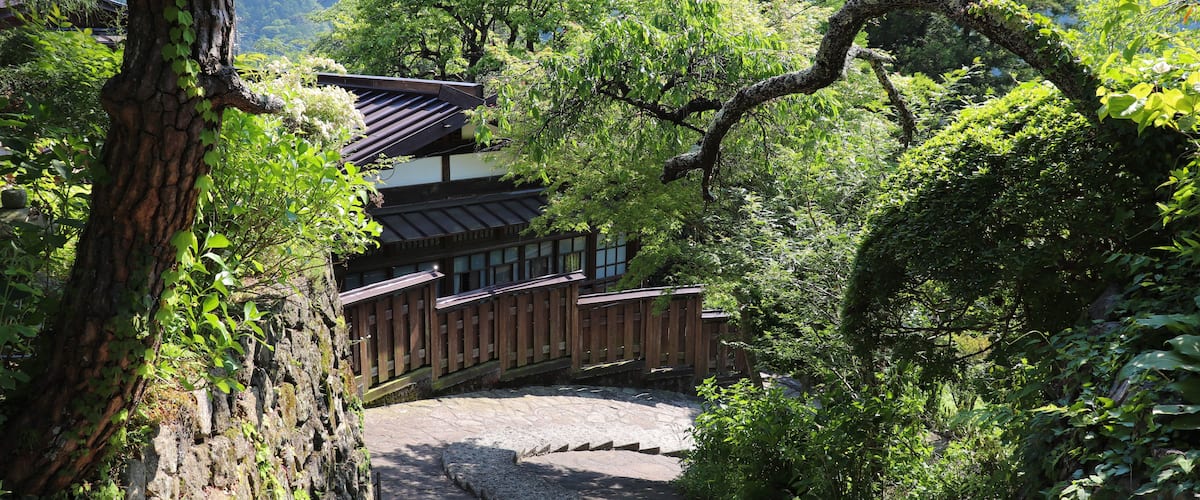 A traditional Japanese building surrounded by lush greenery and a stone pathway.