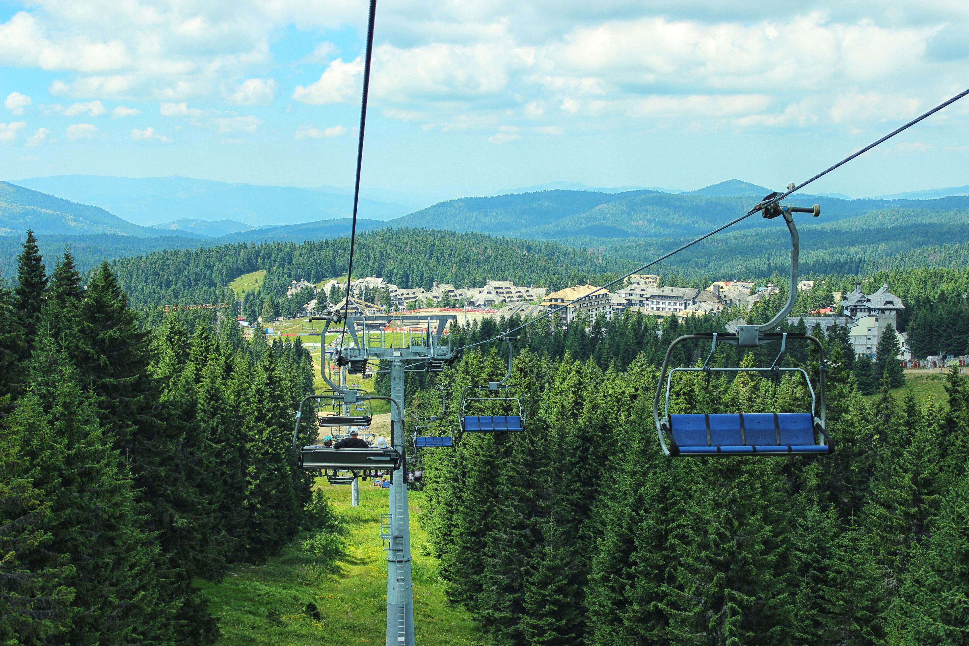 A ski lift with cabins in a forested mountain area, with buildings and a town in the background.