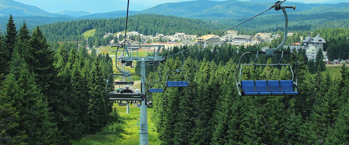 A ski lift with cabins in a forested mountain area, with buildings and a town in the background.