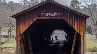 A wooden covered bridge with a sign reading "Watson Mill Bridge EST. 1885".
