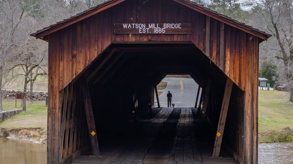 A wooden covered bridge with a sign reading "Watson Mill Bridge EST. 1885".