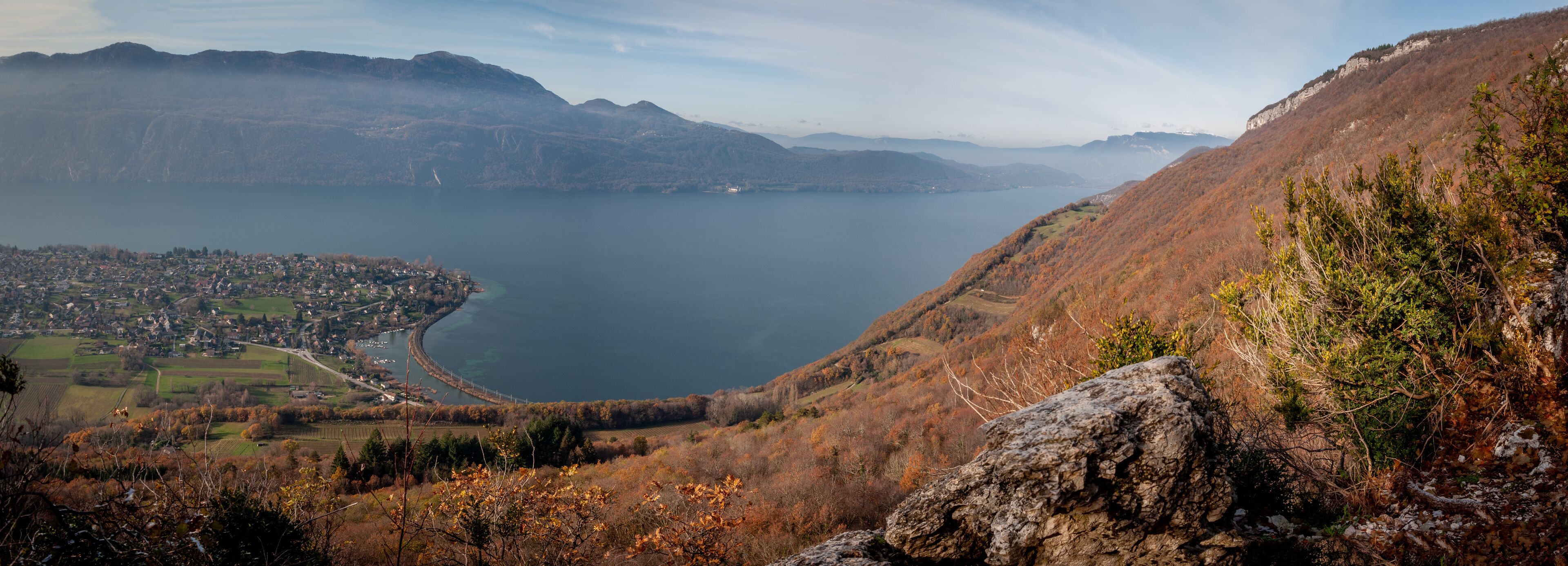 A panoramic view of a lake surrounded by mountains, a town in the valley, and autumn foliage.