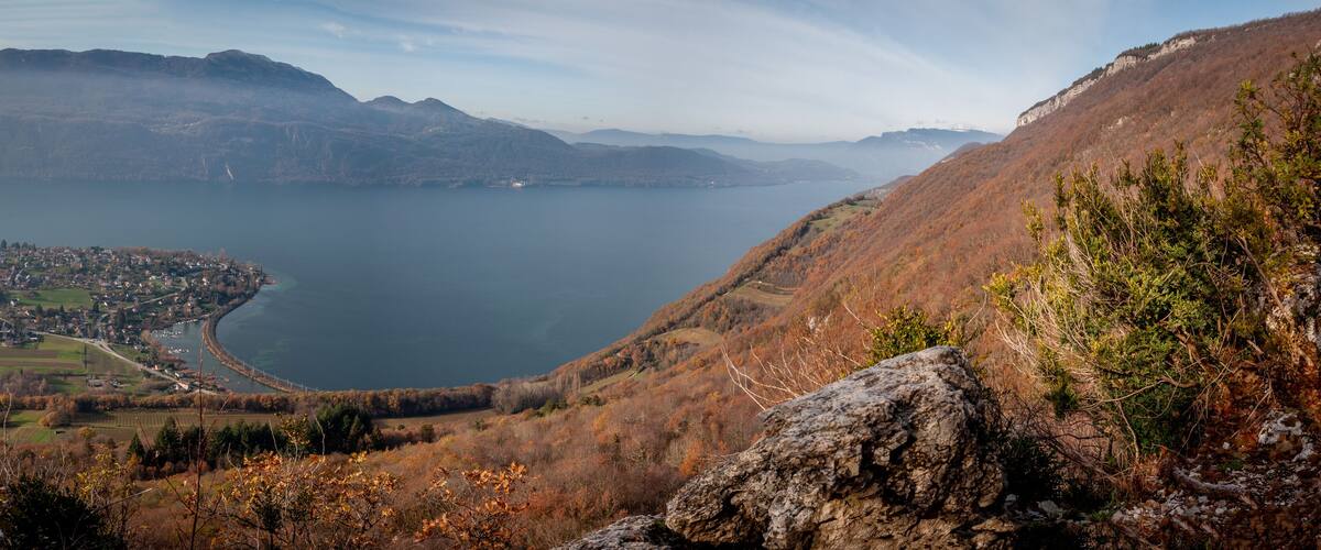 A panoramic view of a lake surrounded by mountains, a town in the valley, and autumn foliage.