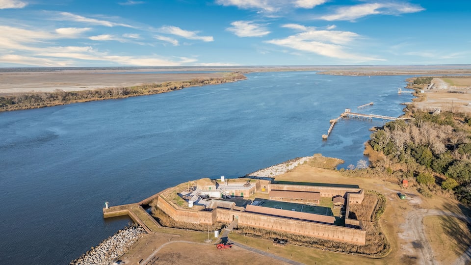 An aerial view of a fortified structure by a river with a bridge and a lighthouse.