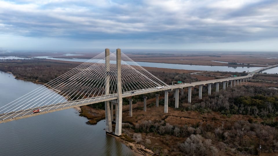 A large suspension bridge over a river, surrounded by fields and trees.