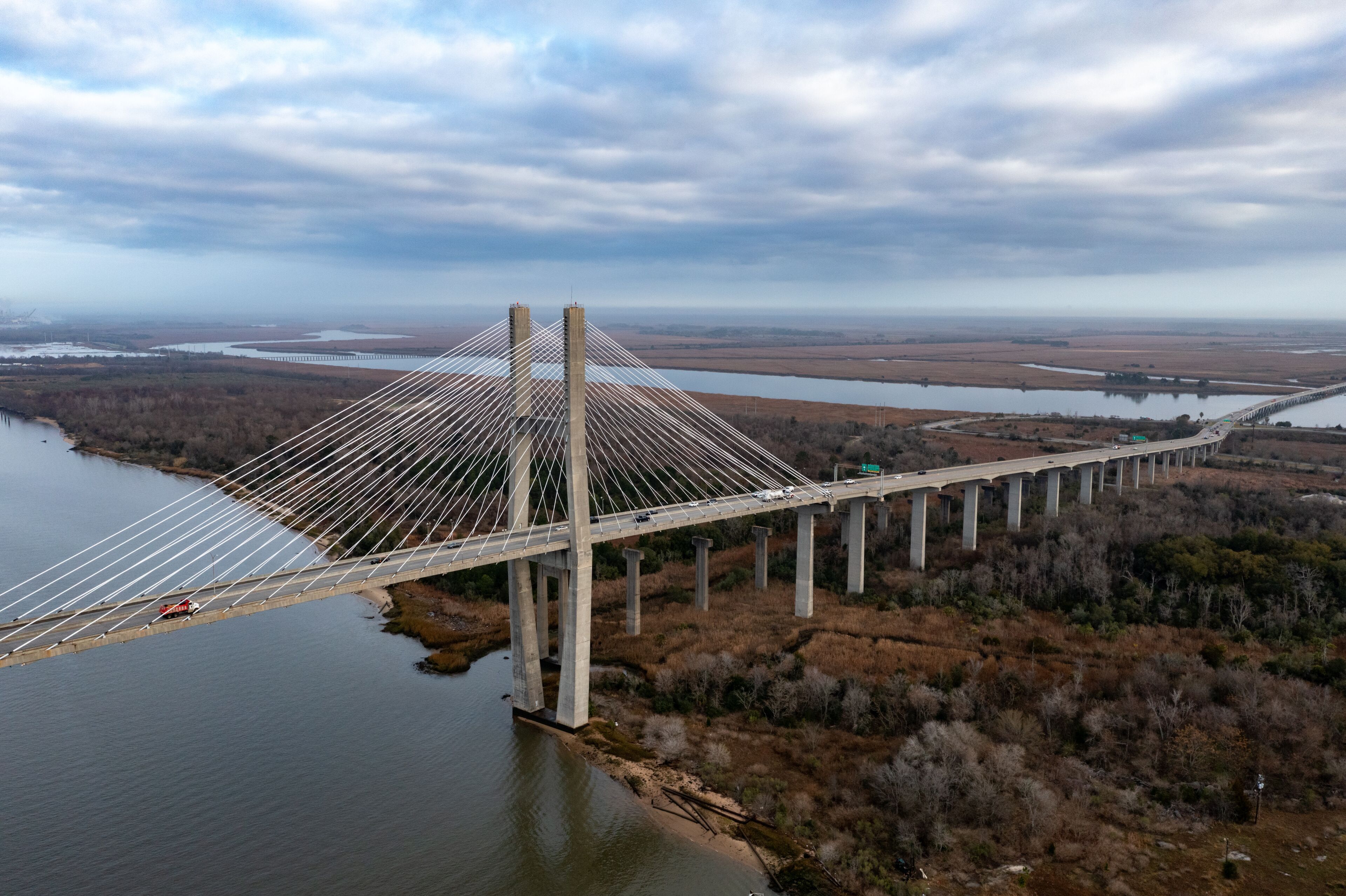 A large suspension bridge over a river, surrounded by fields and trees.