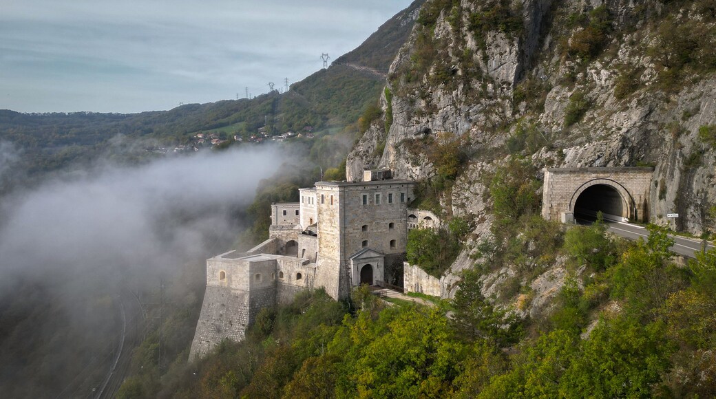 Aerial view of Fort l'Ecluse nestled against a rocky cliffside with a road tunnel and low-hanging mist in the valley, Leaz, Auvergne-Rhone-Alpes, France.