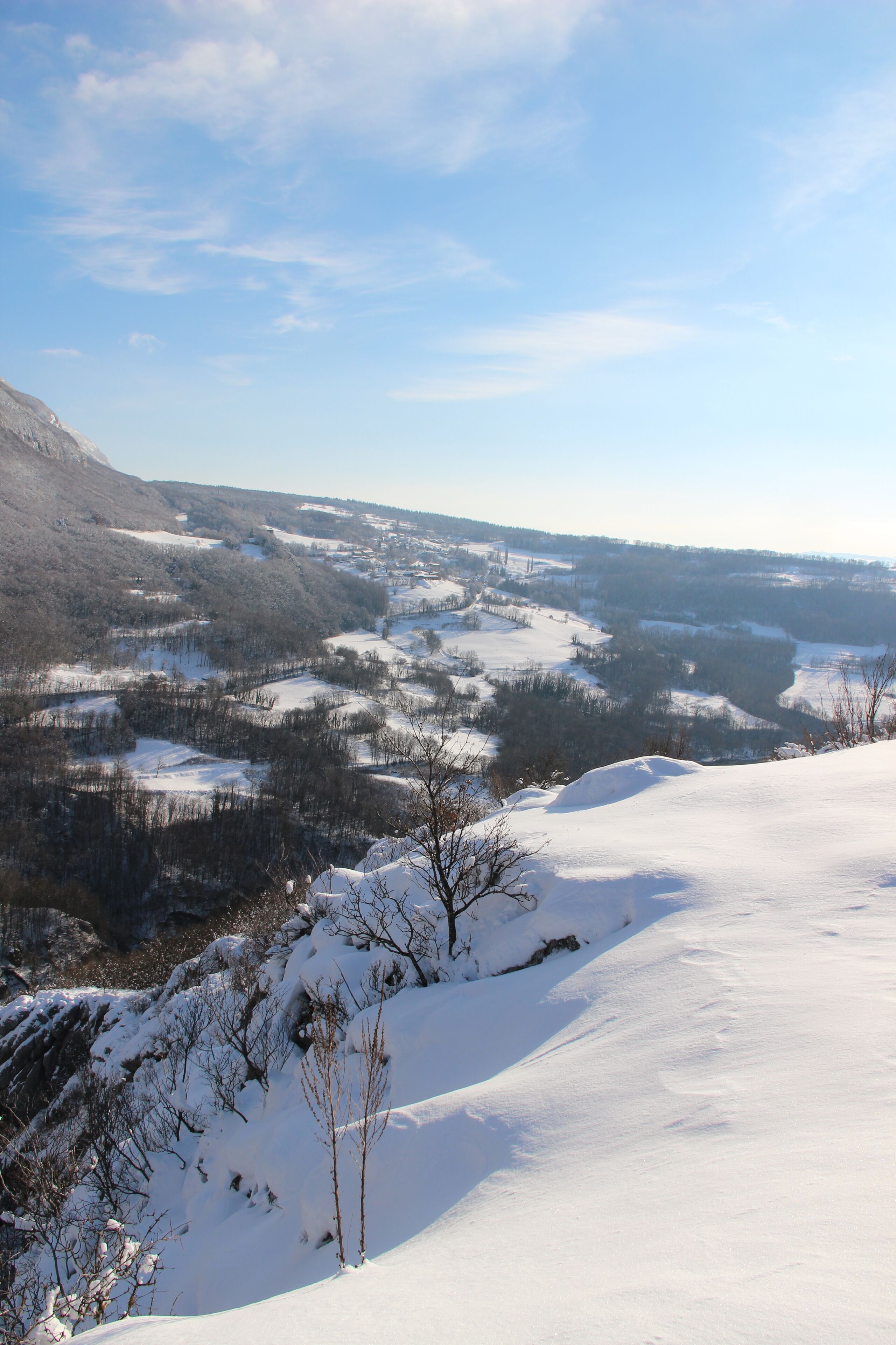 A snow-covered landscape with a valley and distant hills.