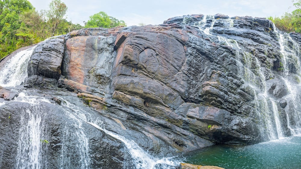 A multi-tiered waterfall cascading over large rocks into a pool, surrounded by lush greenery.