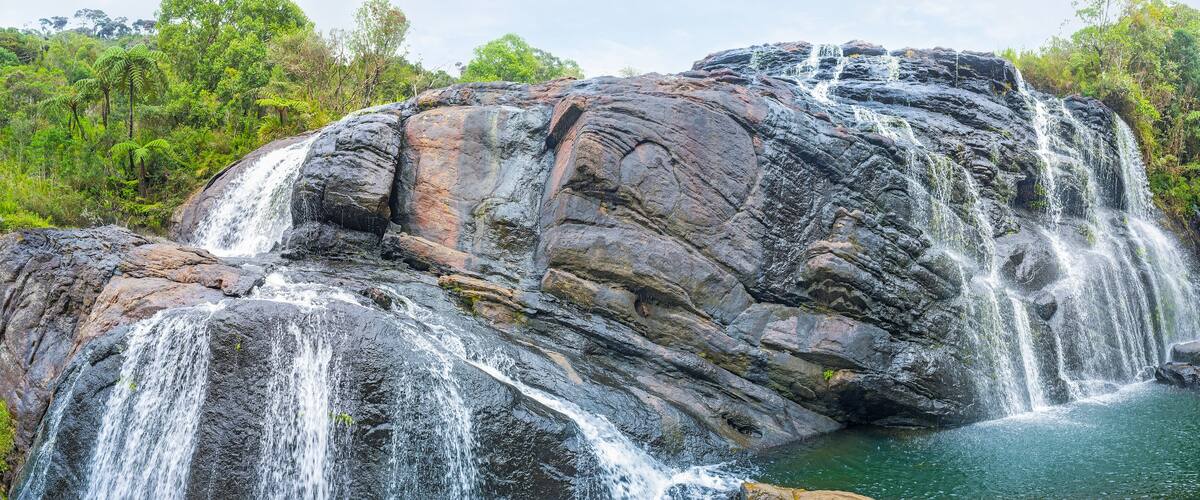 A multi-tiered waterfall cascading over large rocks into a pool, surrounded by lush greenery.