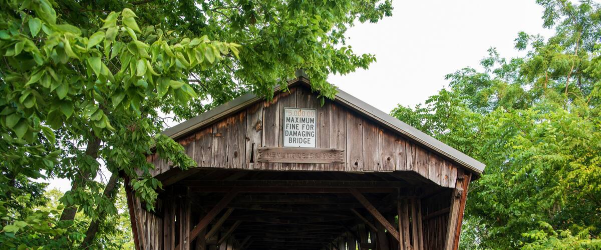 A wooden covered bridge with a sign indicating a maximum fine for damaging it.