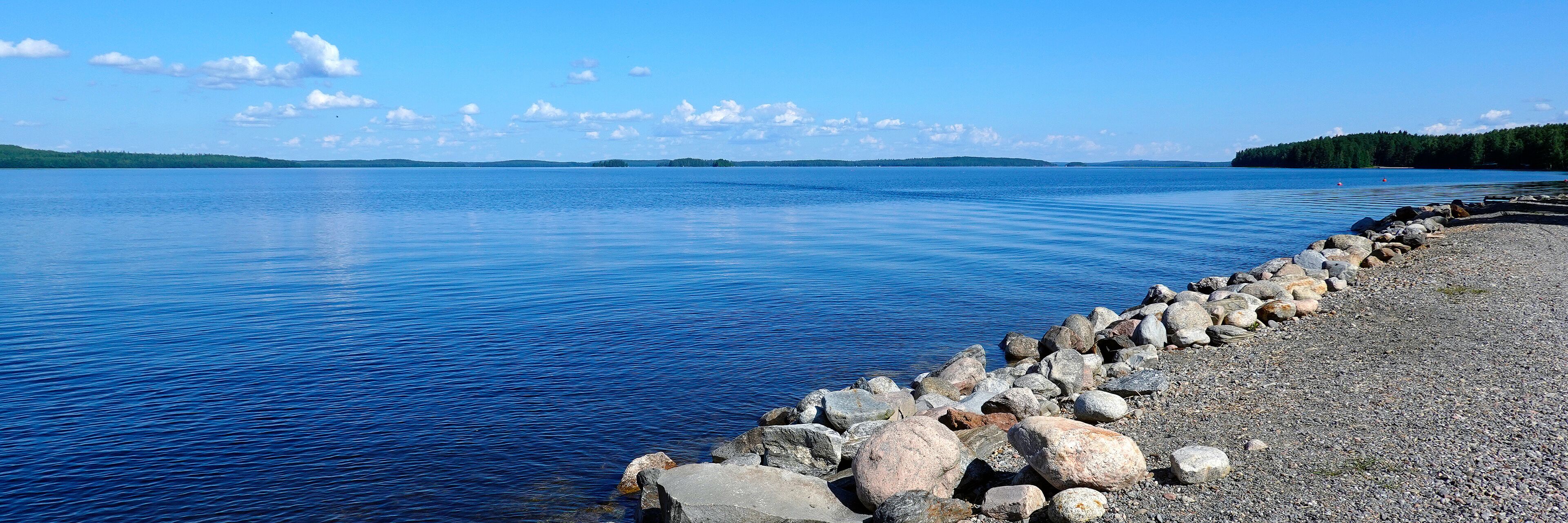 A calm lake with a rocky shoreline and distant forested hills.
