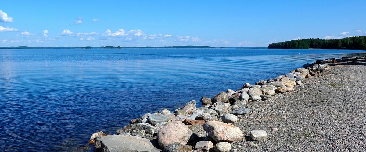 A calm lake with a rocky shoreline and distant forested hills.