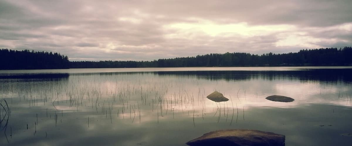 A calm lake with two prominent rocks in the center and a forested shoreline in the background.