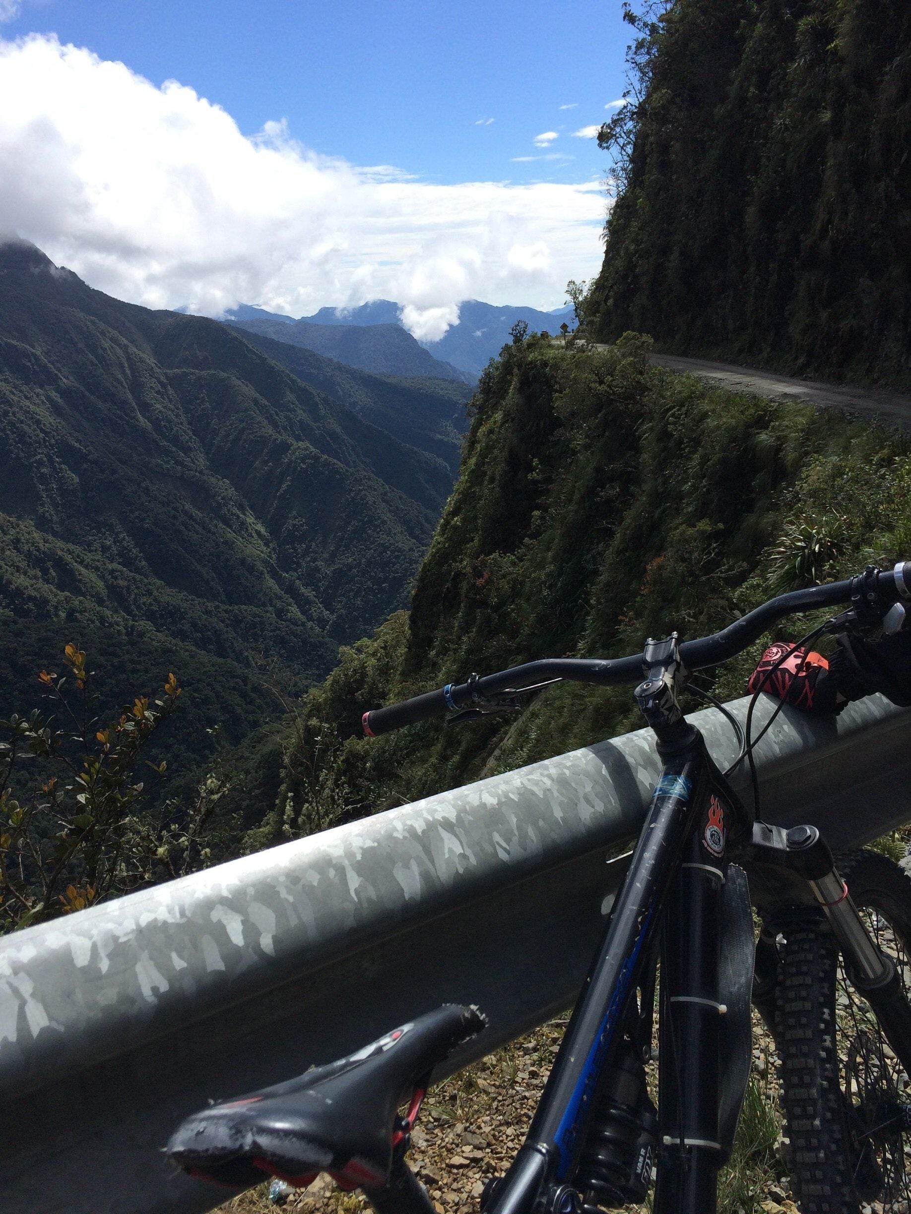 A mountain bike parked on a guardrail overlooking a valley with lush greenery and distant mountains.
