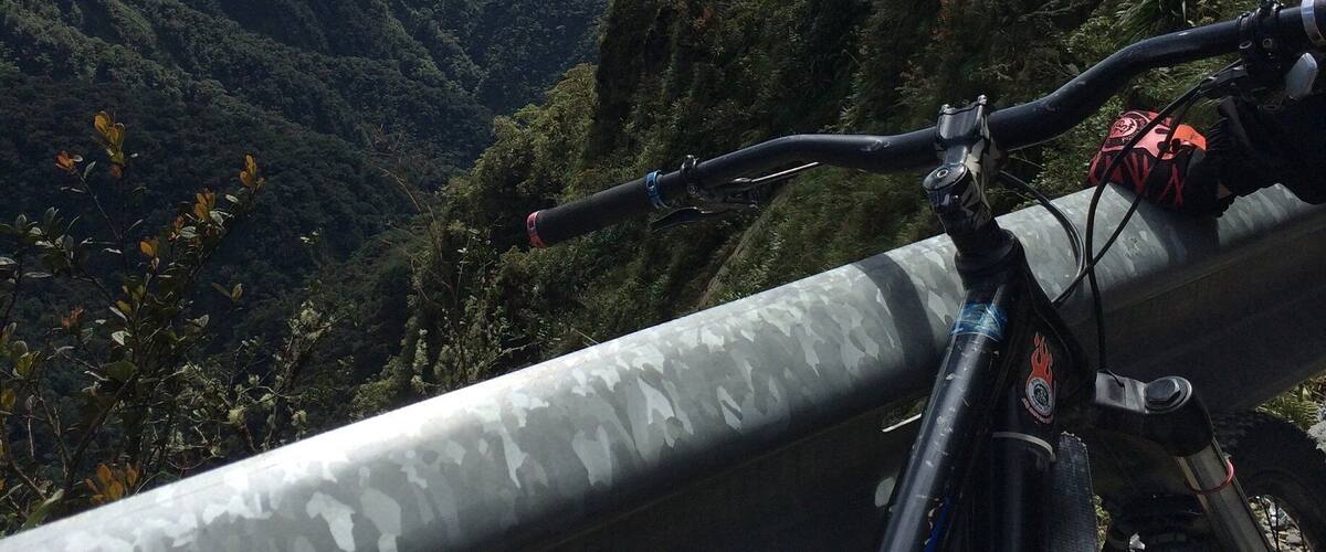 A mountain bike parked on a guardrail overlooking a valley with lush greenery and distant mountains.