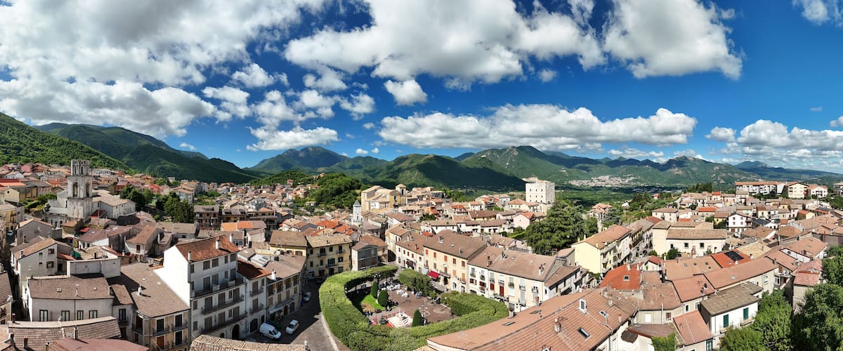 A town with historic buildings, a central square, and mountains in the background.