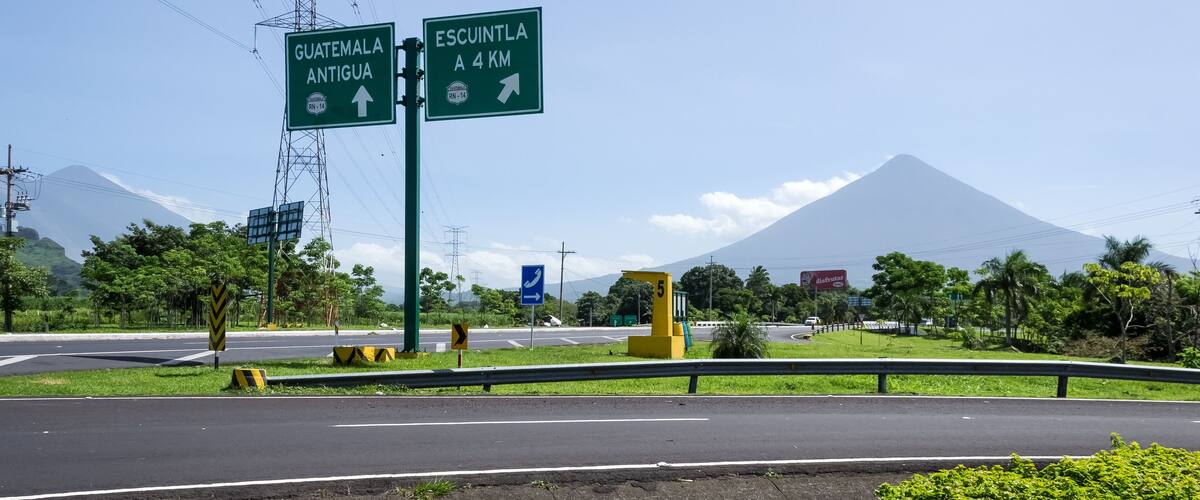 A road sign indicating Guatemala Antigua and Escuintla, with a mountain in the background.