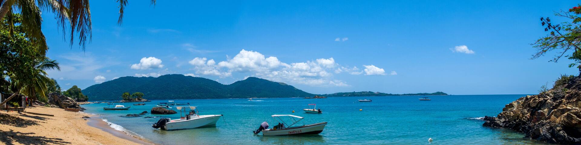 Coastline / Beach of Nosy Komba Island lined with palm trees and pirogue Madagascar close to Nosy Be