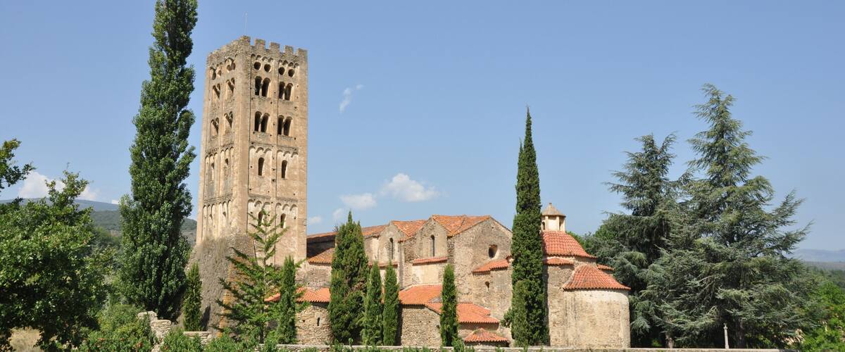 A historic stone tower and buildings with red-tiled roofs, surrounded by greenery and cypress trees.