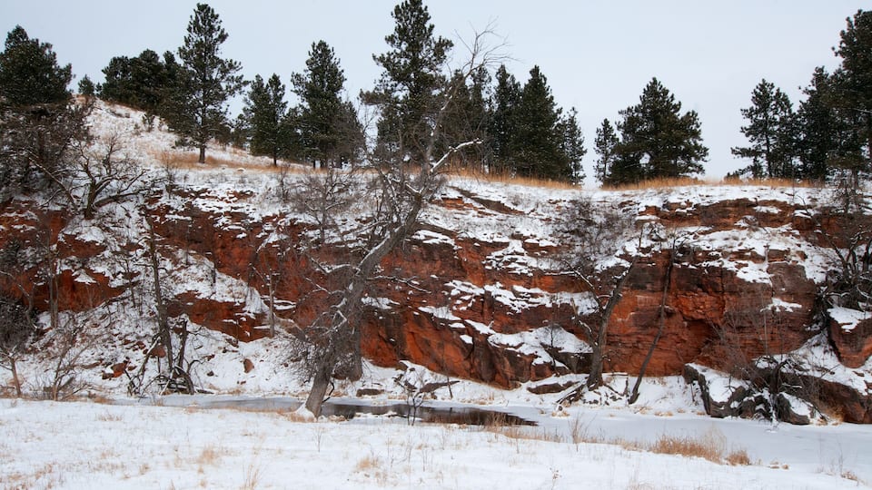 A snow-covered landscape with red rock formations and sparse trees.