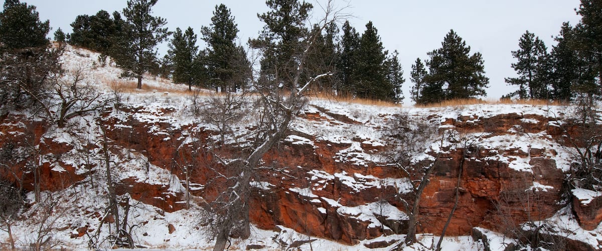 A snow-covered landscape with red rock formations and sparse trees.