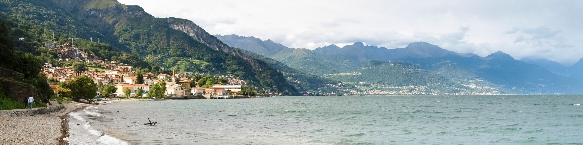 A coastal town with buildings on a hillside, a beach, and mountains in the background.