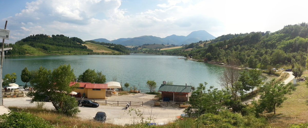 A lake surrounded by hills and trees. There is a small building with a red roof near the water.