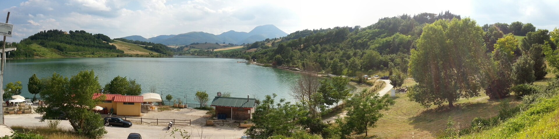 A lake surrounded by hills and trees. There is a small building with a red roof near the water.
