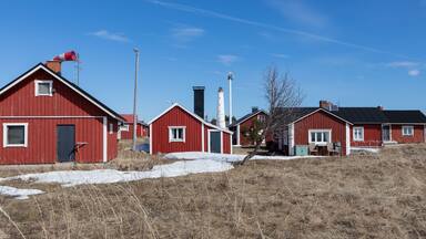 A cluster of red wooden buildings with a lighthouse in the background.