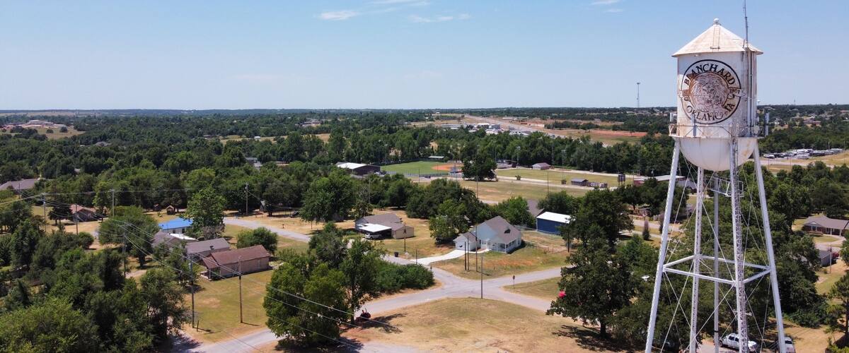 A water tower with a clock, surrounded by a rural landscape with houses and trees.