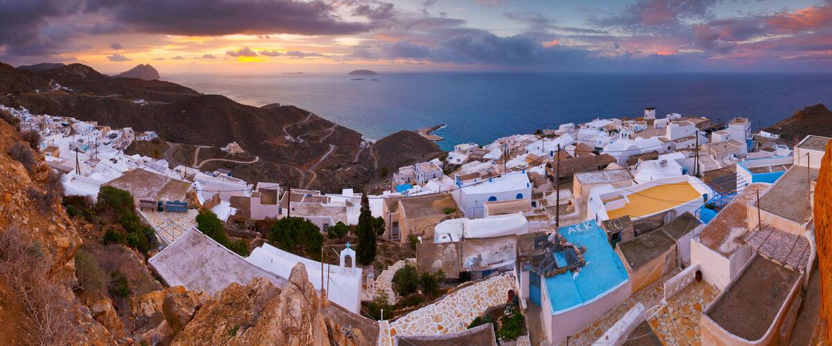 A coastal village with white buildings, winding roads, and a view of the sea at sunset.