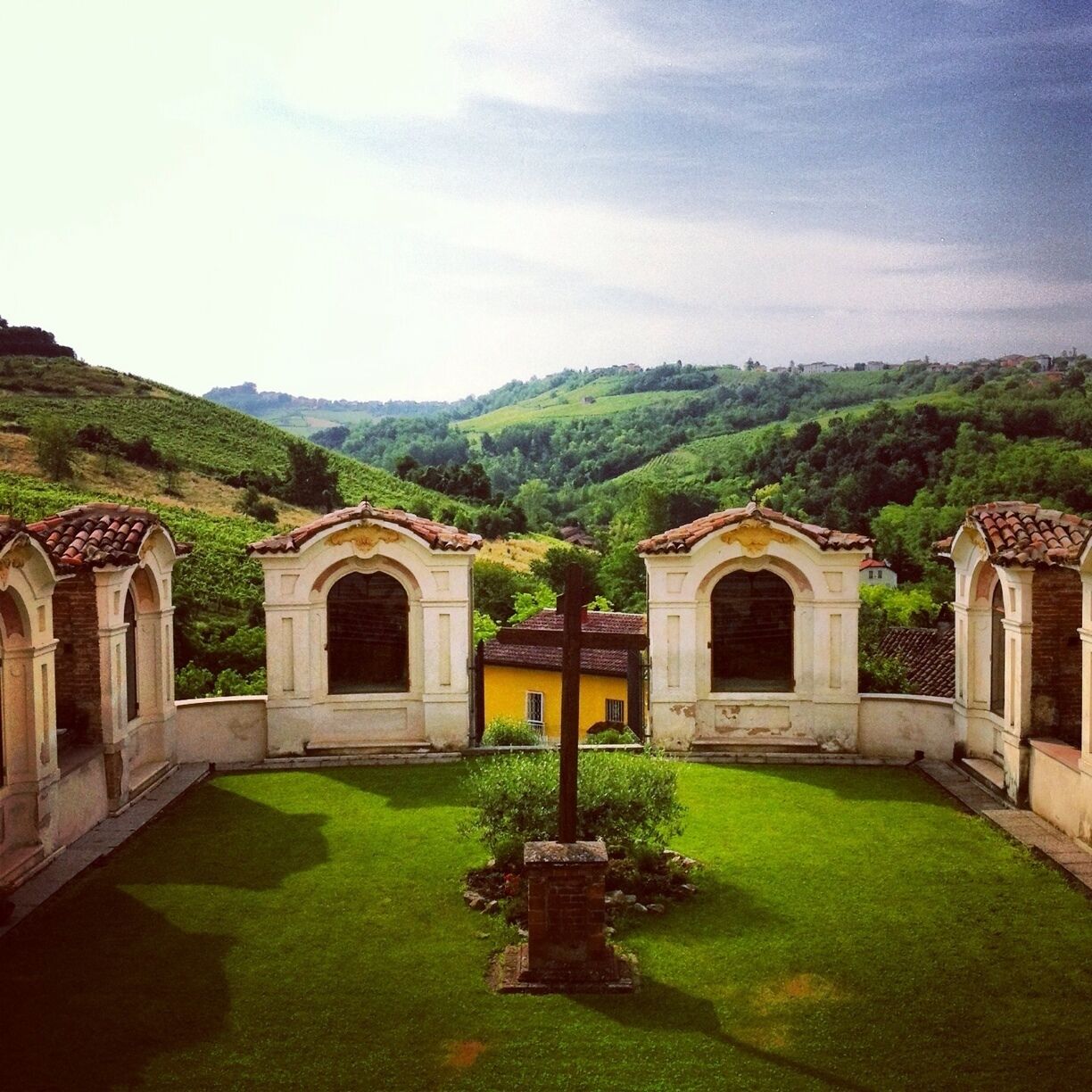 A courtyard with arched structures, a central pillar, and a hillside in the background.