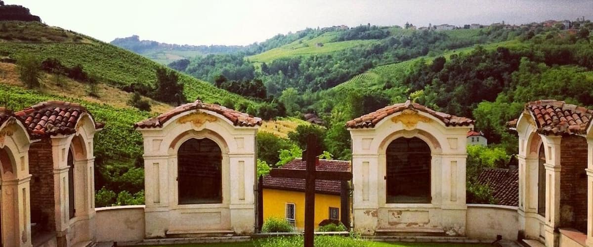 A courtyard with arched structures, a central pillar, and a hillside in the background.