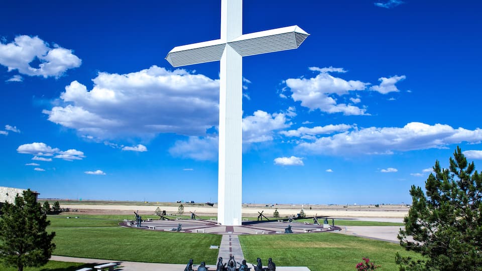 A large white cross monument in a park with green grass and trees.