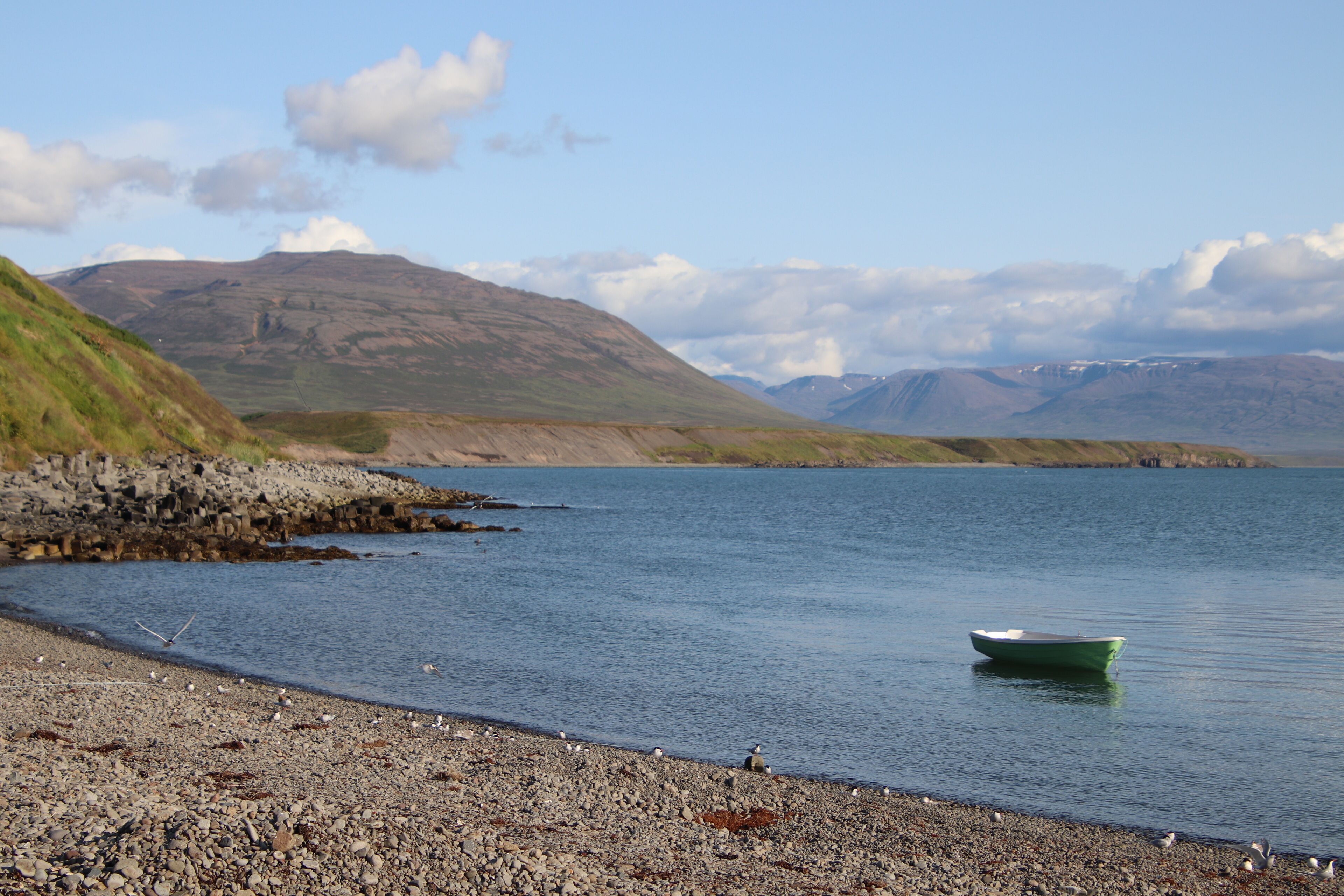 A calm lake with a small boat, rocky shore, and distant mountains.