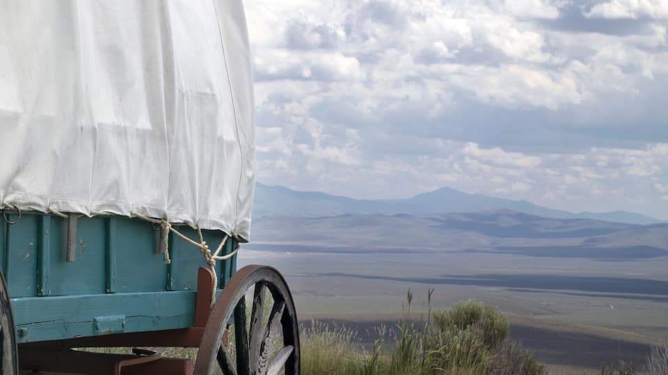 A covered wagon with a white canvas, wooden wheels, and a rope tied to the canvas.