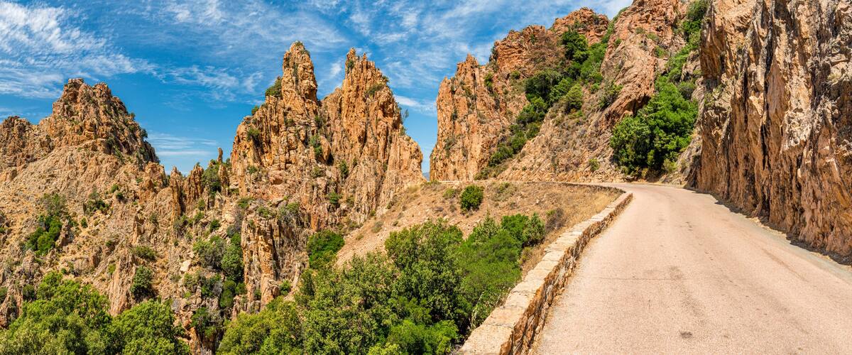A winding mountain road surrounded by rugged cliffs and sparse vegetation.