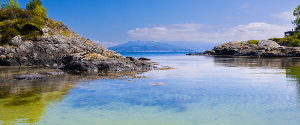 A calm lake surrounded by rocky shores with sparse vegetation and distant mountains.