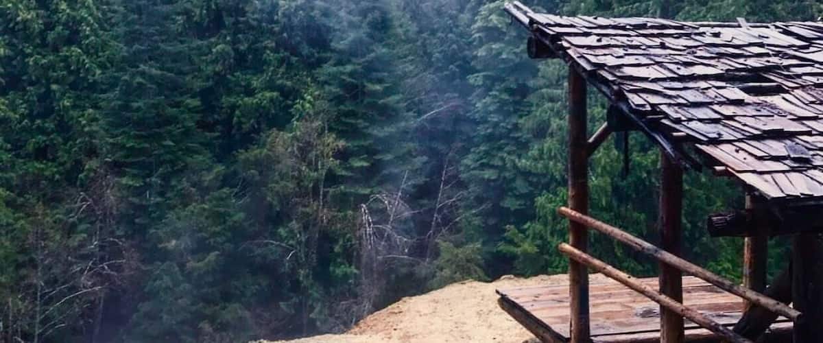 A wooden structure overlooking a forested valley with a small pond.