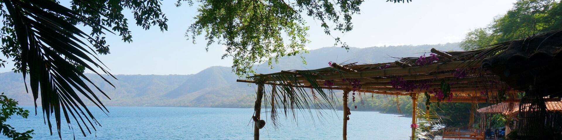 A wooden deck overlooking a calm lake, surrounded by lush greenery and mountains in the background.