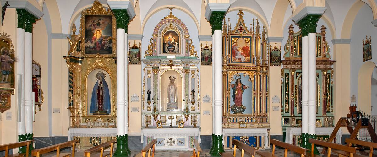 An ornate church interior with multiple altars, wooden pews, and religious paintings.