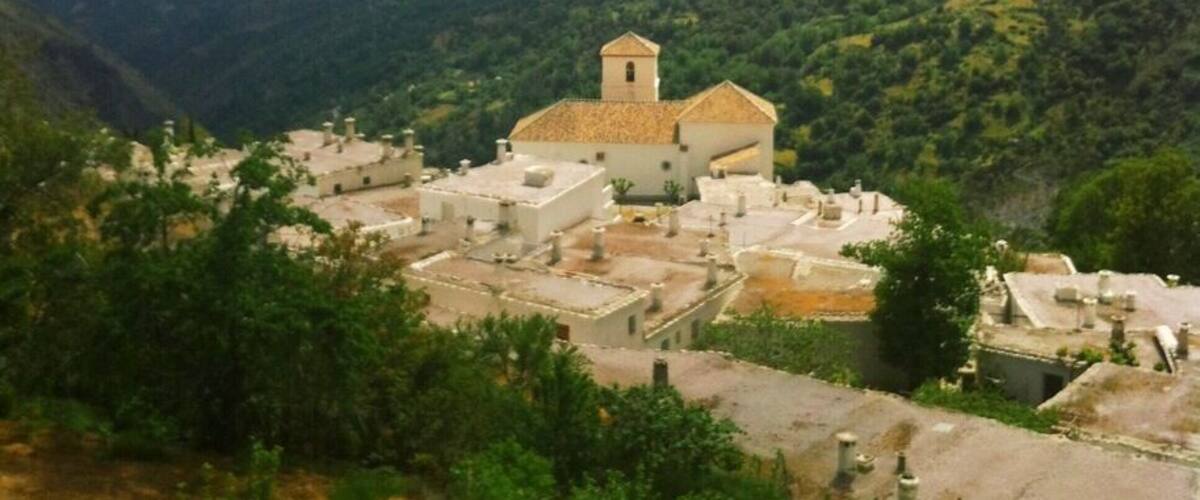 A village with a prominent church surrounded by lush green hills.