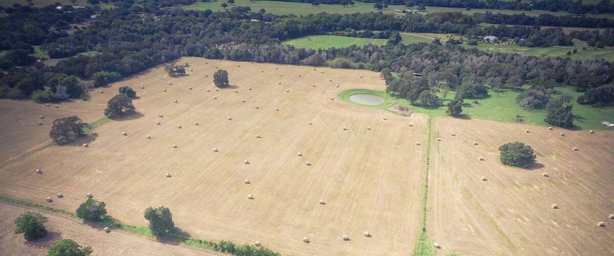 Vintage aerial prairie field at Texas Hill Country sunny day. Bale hay bales strewn across the farm after harvest. Rural landscape pasture Texas ranch farmland in summer time. Agriculture background
