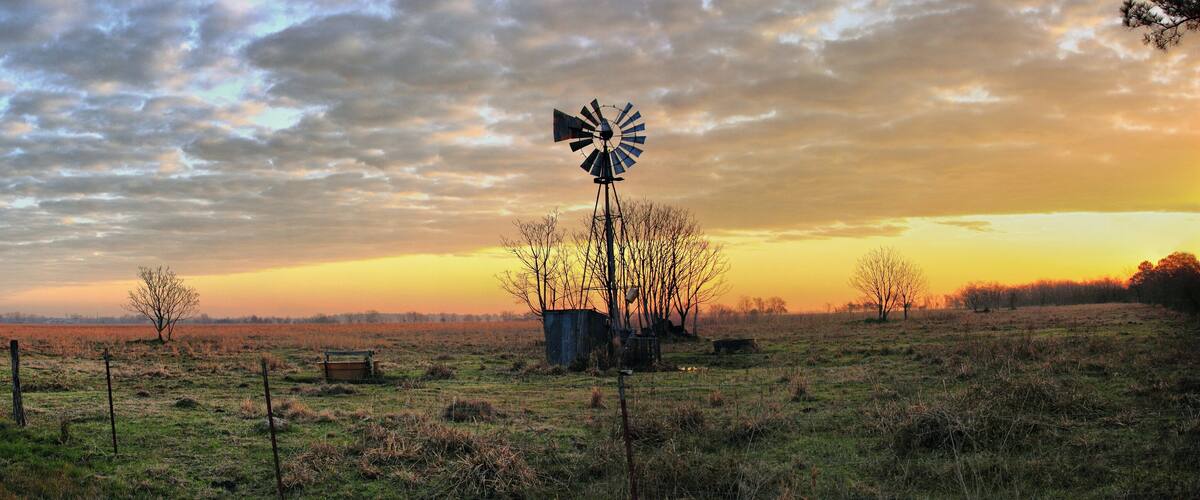A windmill in a field with a sunset in the background.