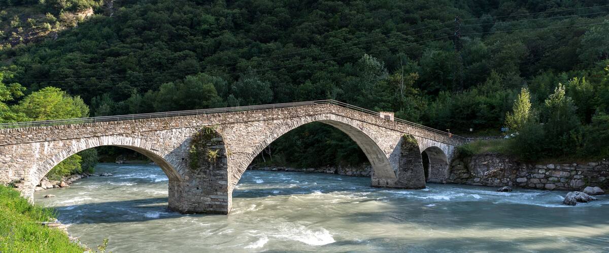 A stone bridge over a river with a forested hillside in the background.