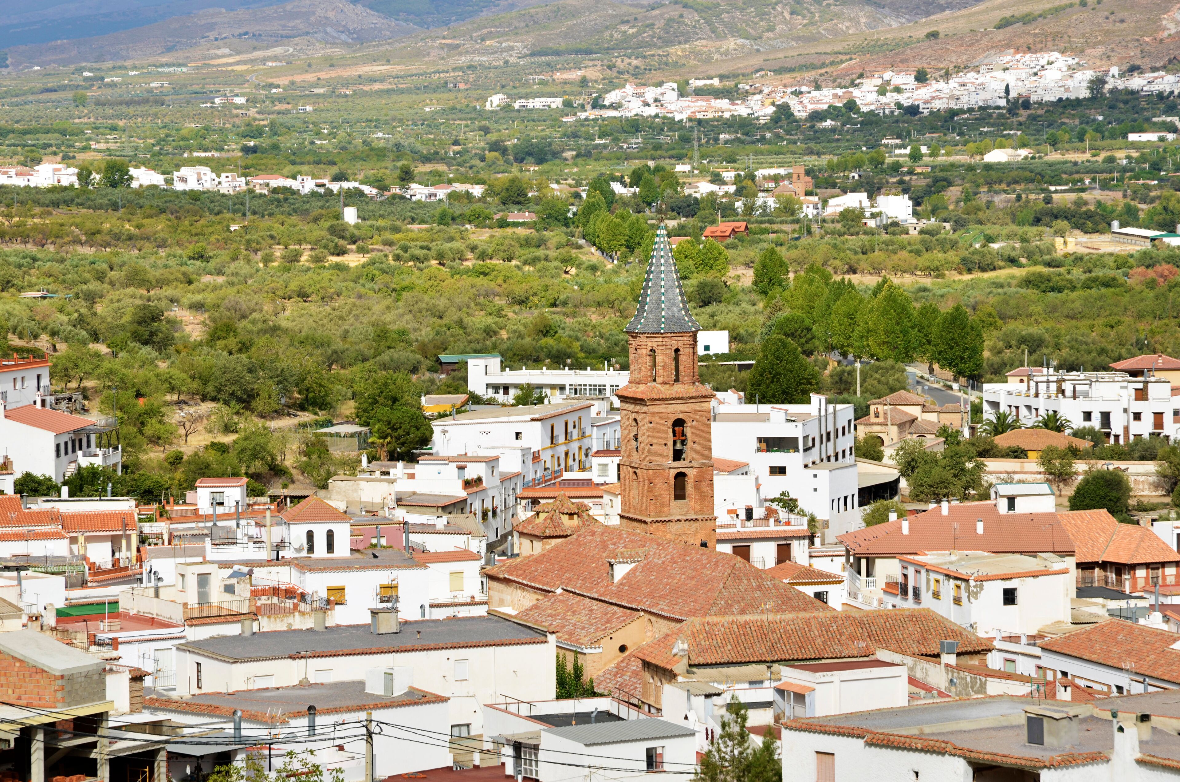 A town with white buildings, a prominent tower, and a hilly landscape in the background.