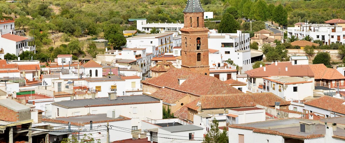 A town with white buildings, a prominent tower, and a hilly landscape in the background.