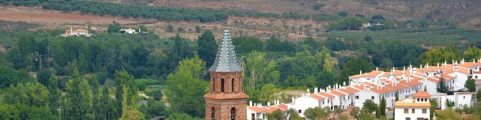 Un pueblo con una imponente torre de iglesia, rodeado de casas escalonadas y abundante vegetación.